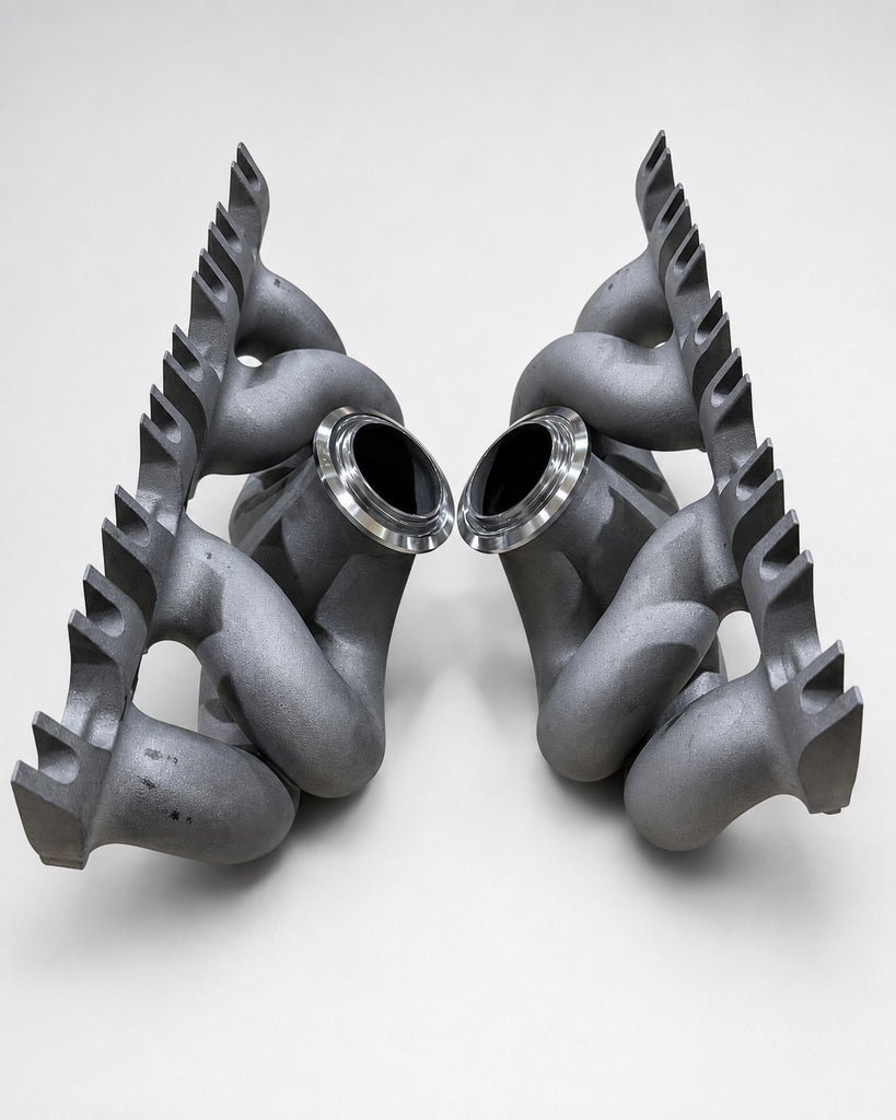 ModalWorks 3D-printed M177 equal-length exhaust manifolds standing upright, showing runner loops and CNC-machined V-band turbo flanges